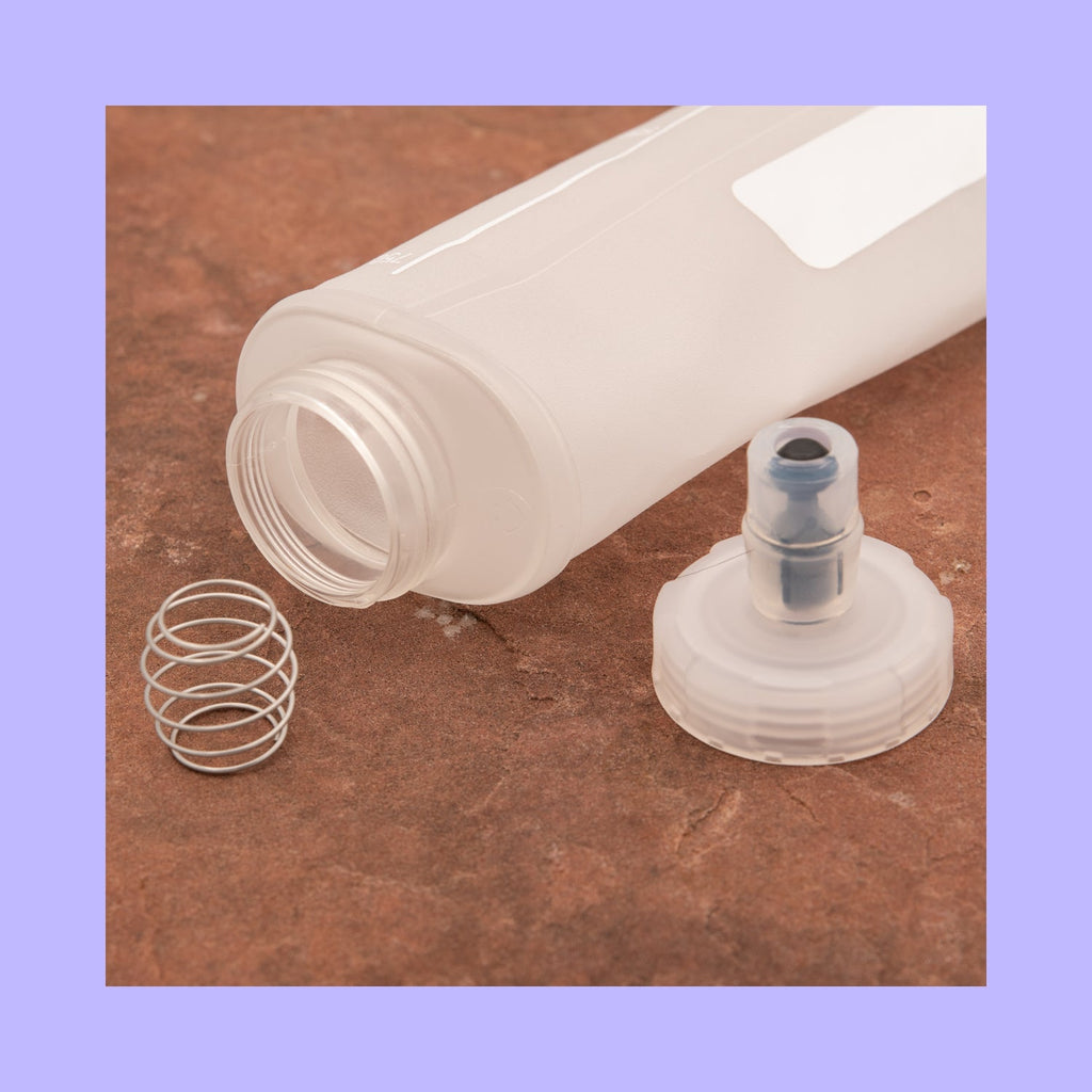 Clear plastic bottle cap, spring, and nozzle on a brown surface with a purple border.