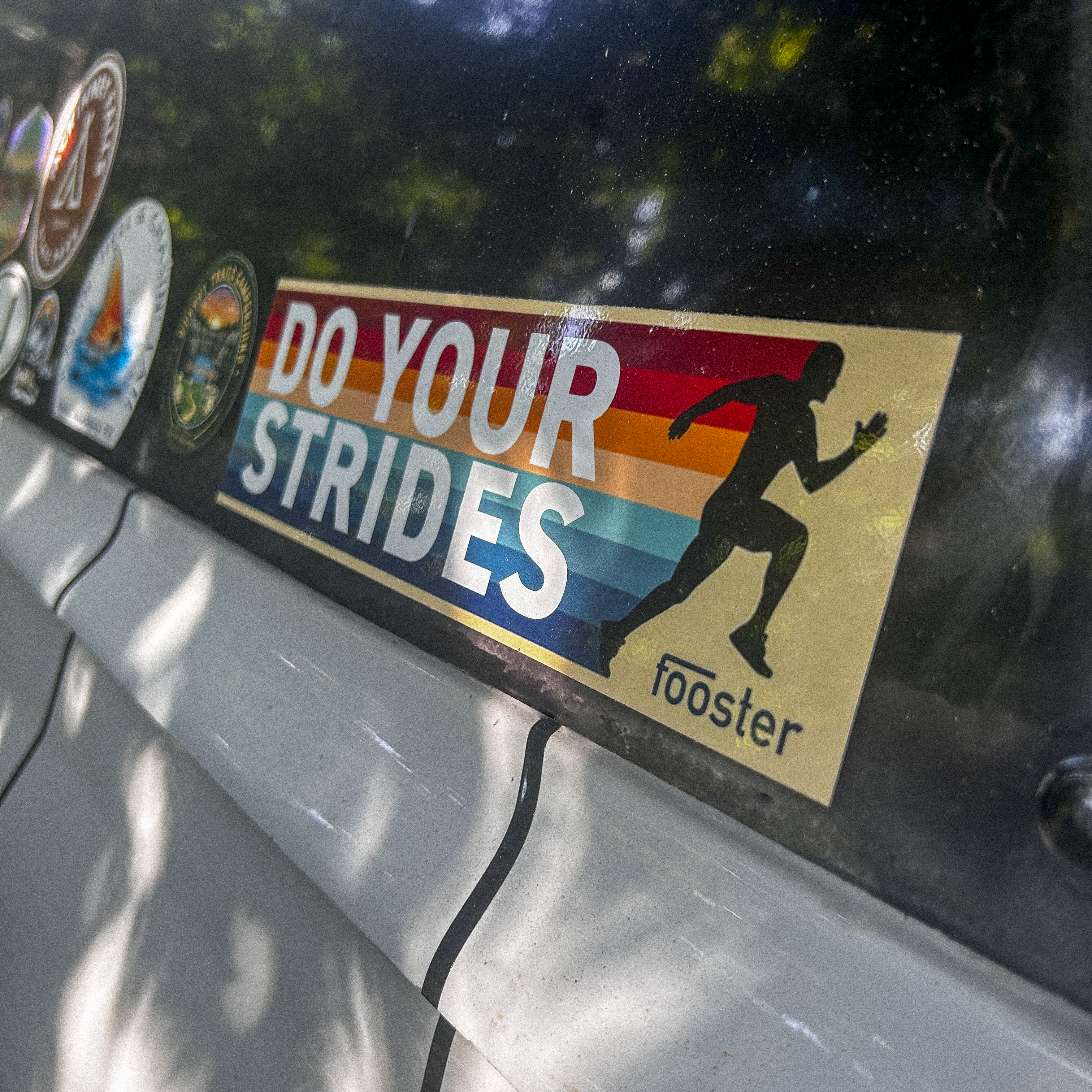 Sticker with 'Do Your Strides' text on a car window with other stickers.